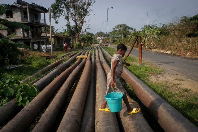 Okrika,Nigéria. Un enfant transporte de l'eau et marche sur les pipelines qui bordent les maisons.