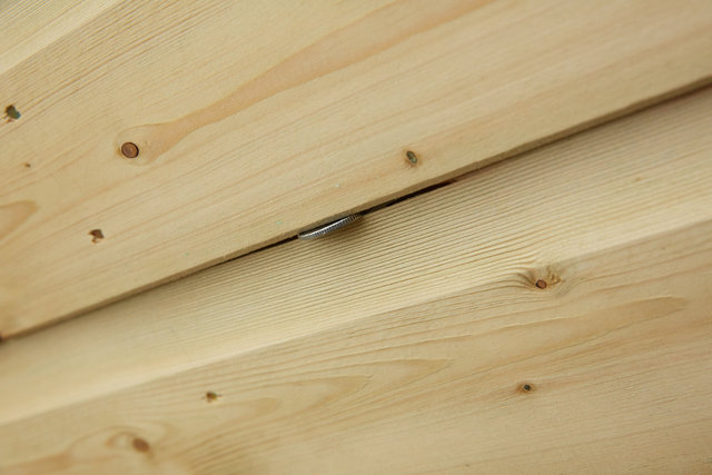 Photo showing gap in tongue and groove of front panel of shed with 10 pence coin inserted to show size of gap