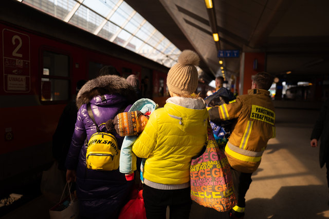 Una donna con il proprio bimbo, arrivati in stazione di Cracovia con un treno proveniente da Psysmuz, viene aiutata con i bagagli da un servizio di guardia polacco per spostarsi nell’area di accoglienza.jpg